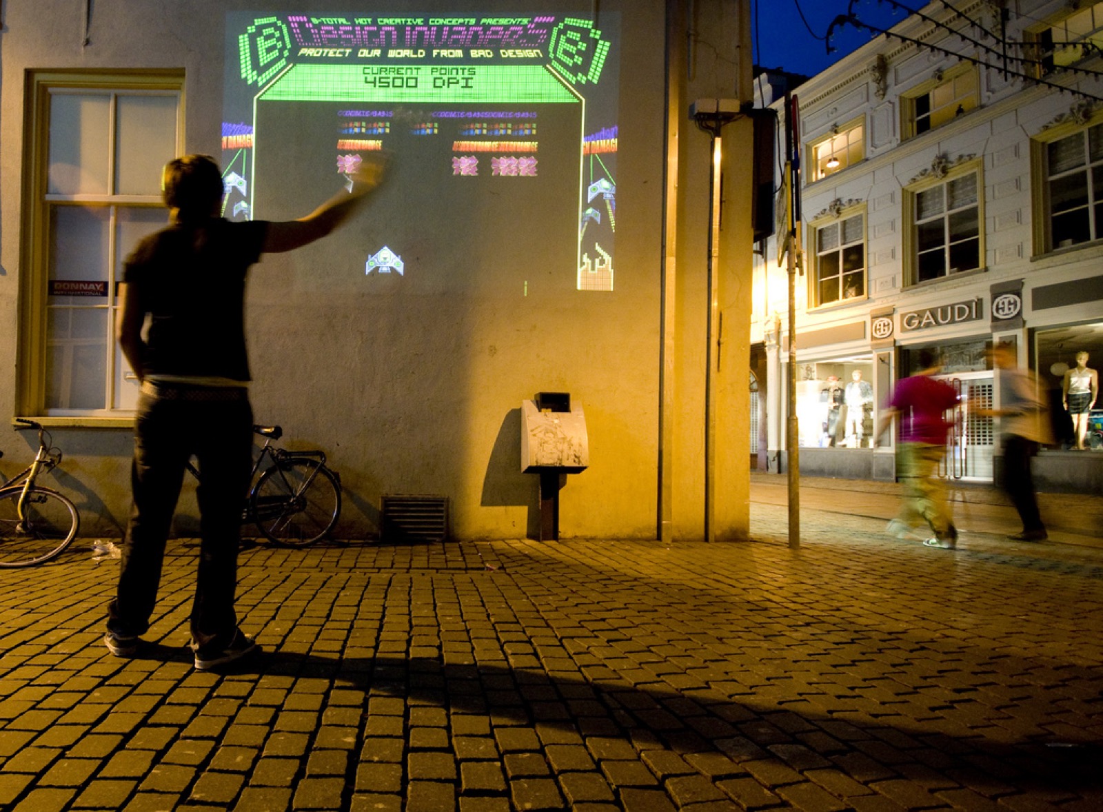 Design Invaders projected onto a building facade at night, played on a cobblestone street